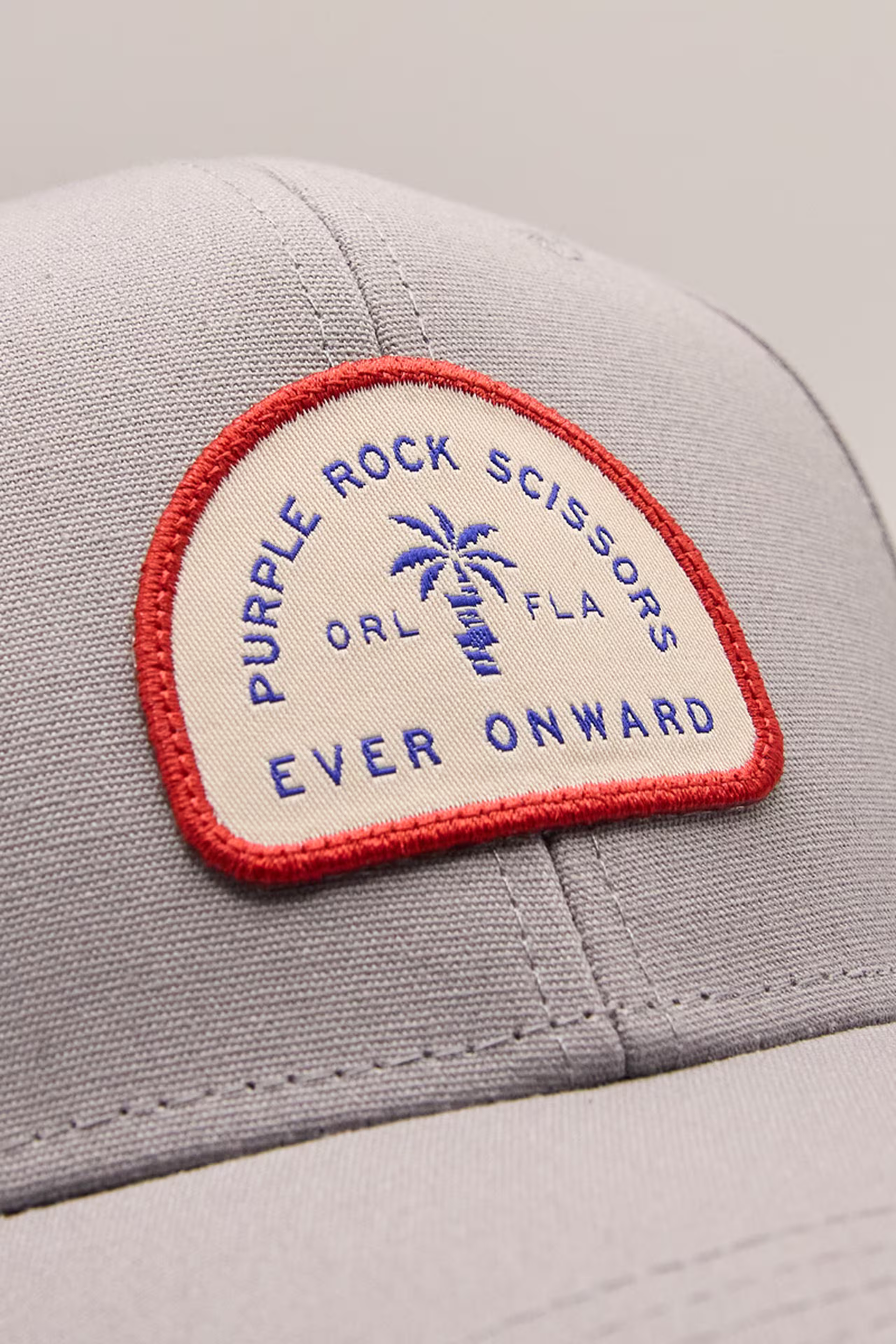 close up of a white and red woven patch with the words purple rock scissors - ever onward and a palm tree illustration
