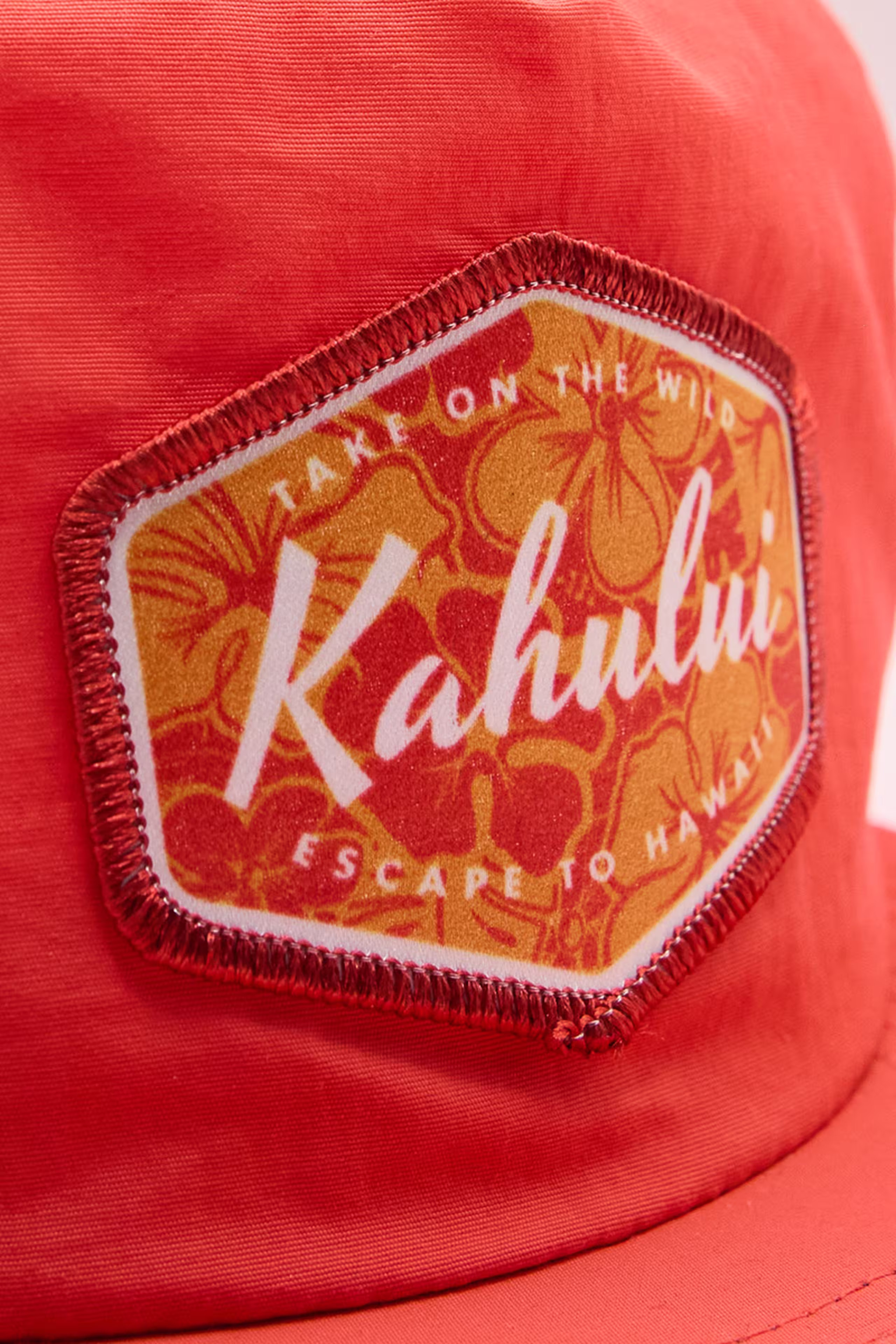 red and orange sublimated patch with flowers and the word kahulu on a red hat