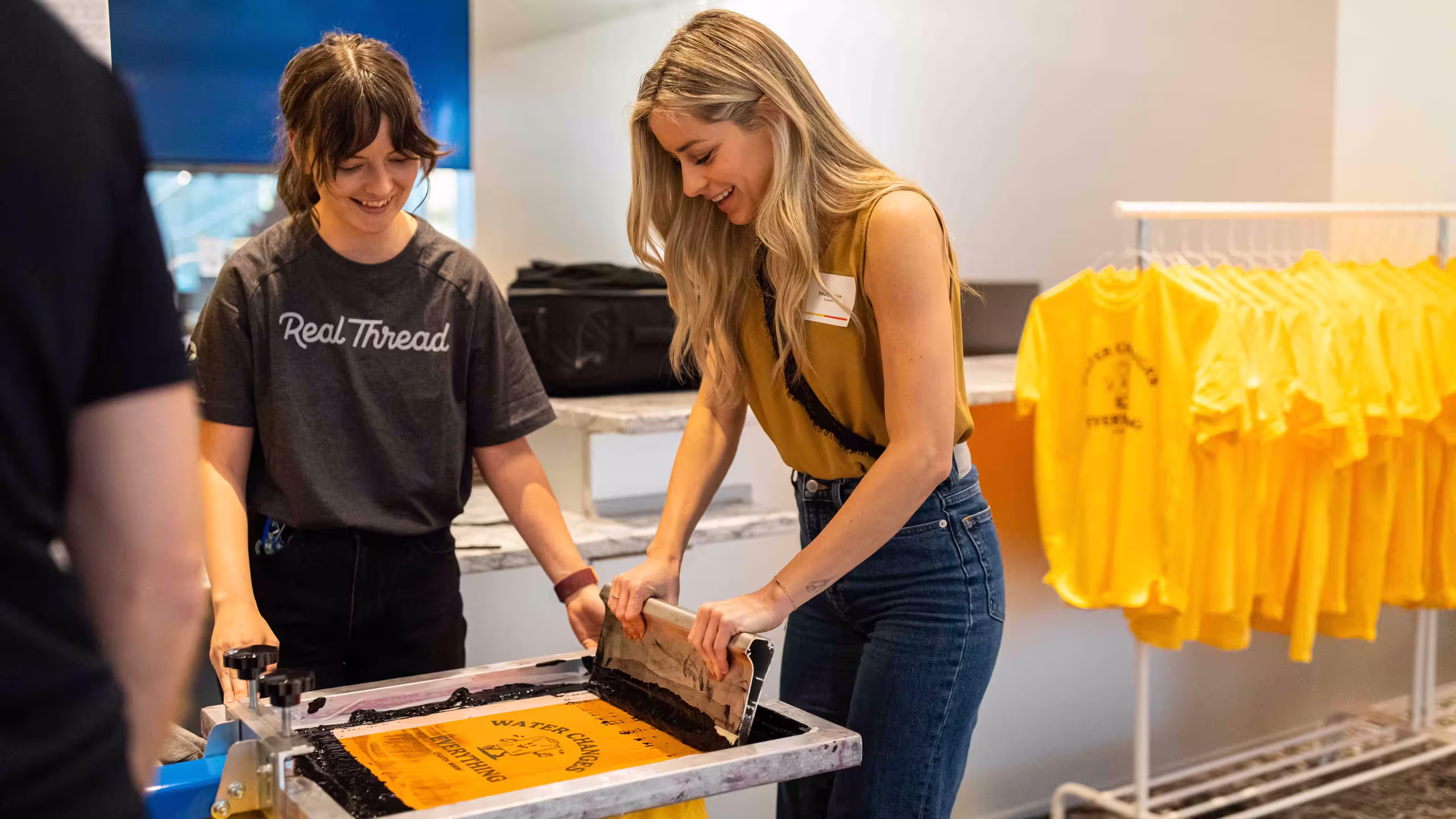 two women screen printing on a yellow shirt