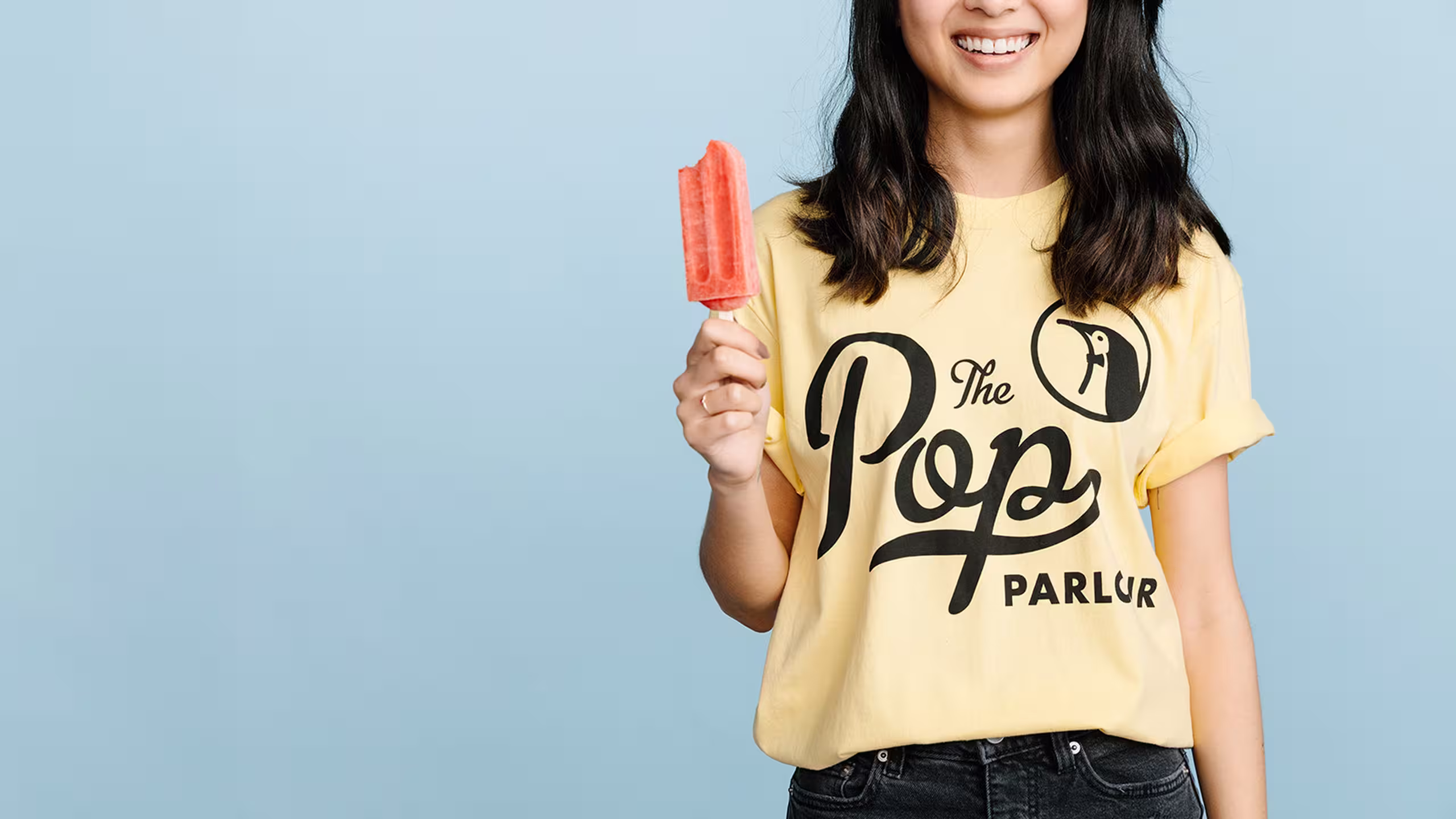 girl wearing a bright yellow shirt holding a popsicle 